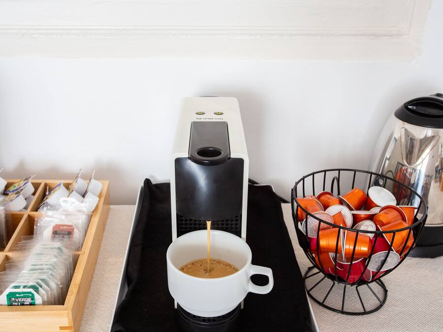 Una macchina per il caffè, una tazza di caffè, un cesto di bicchieri arancioni e una scatola di capsule di caffè su un tavolo.