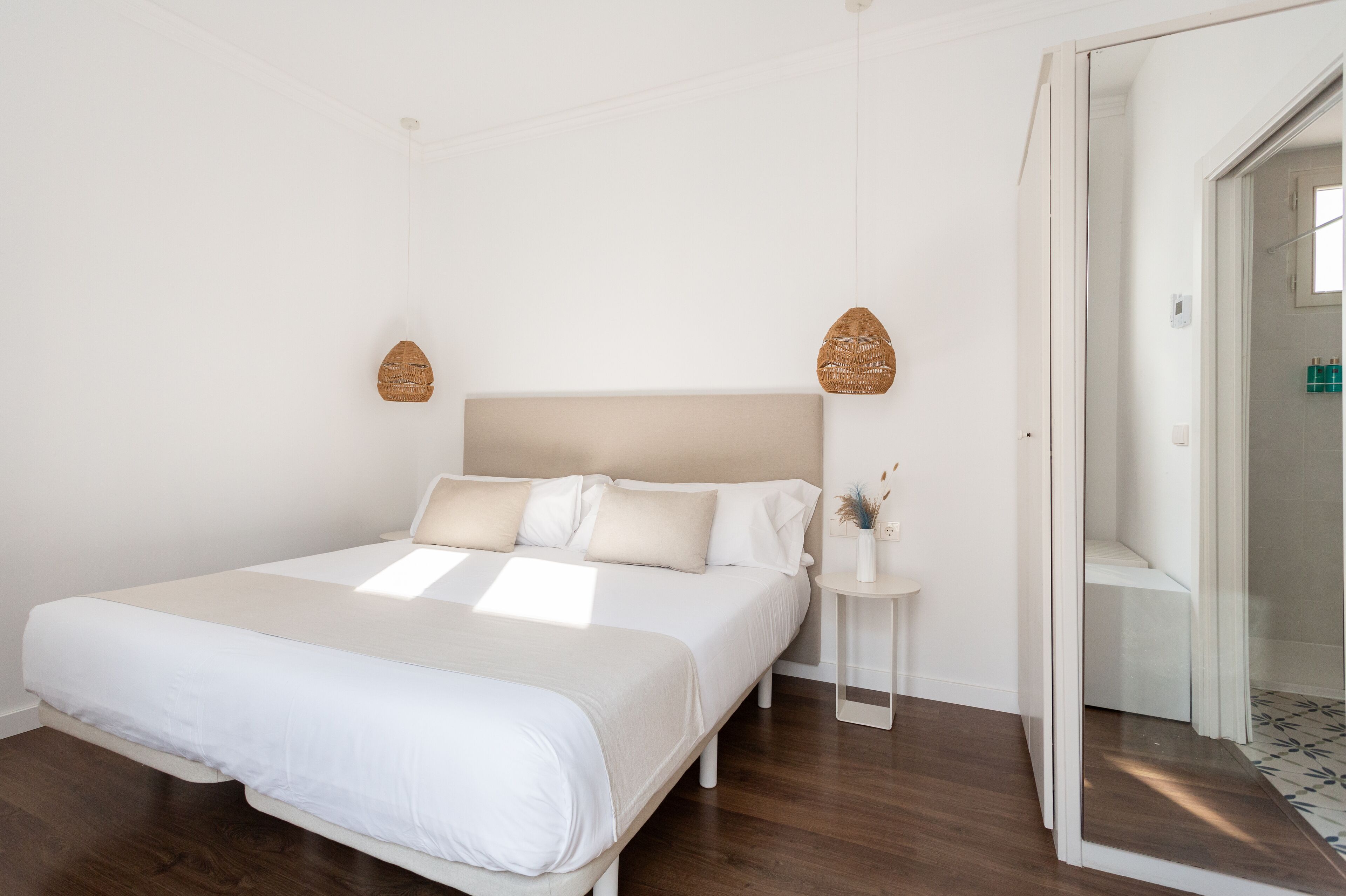 A bedroom with a large bed, a bedside table with a vase, and a door leading to a bathroom.