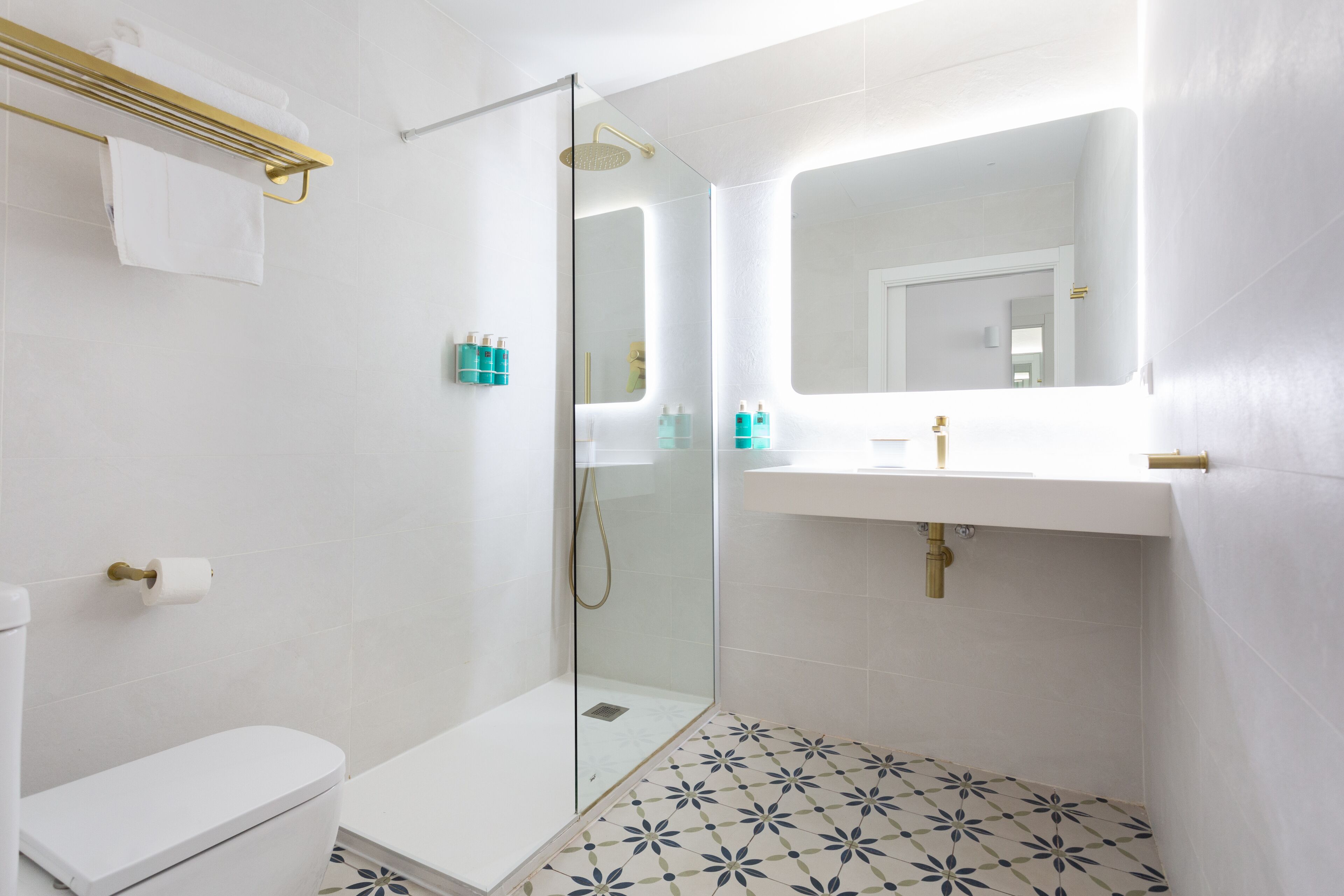 A modern bathroom with a glass-enclosed shower, white fixtures, and patterned floor tiles.