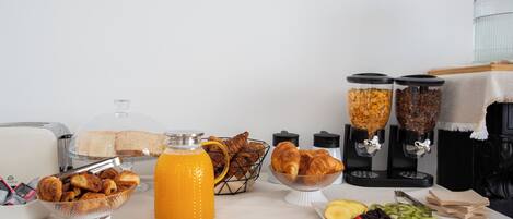 A breakfast buffet with various food items, including fruits, pastries, and a juice dispenser.