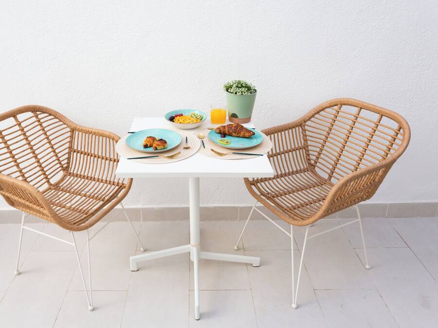 A dining table with two wicker chairs, a bowl of fruit, a croissant, and a glass of orange juice.
