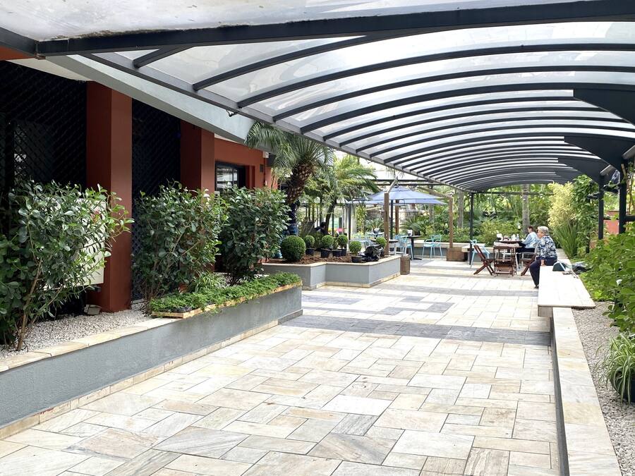 A covered outdoor area with tiled flooring, planters with various plants, and outdoor seating.