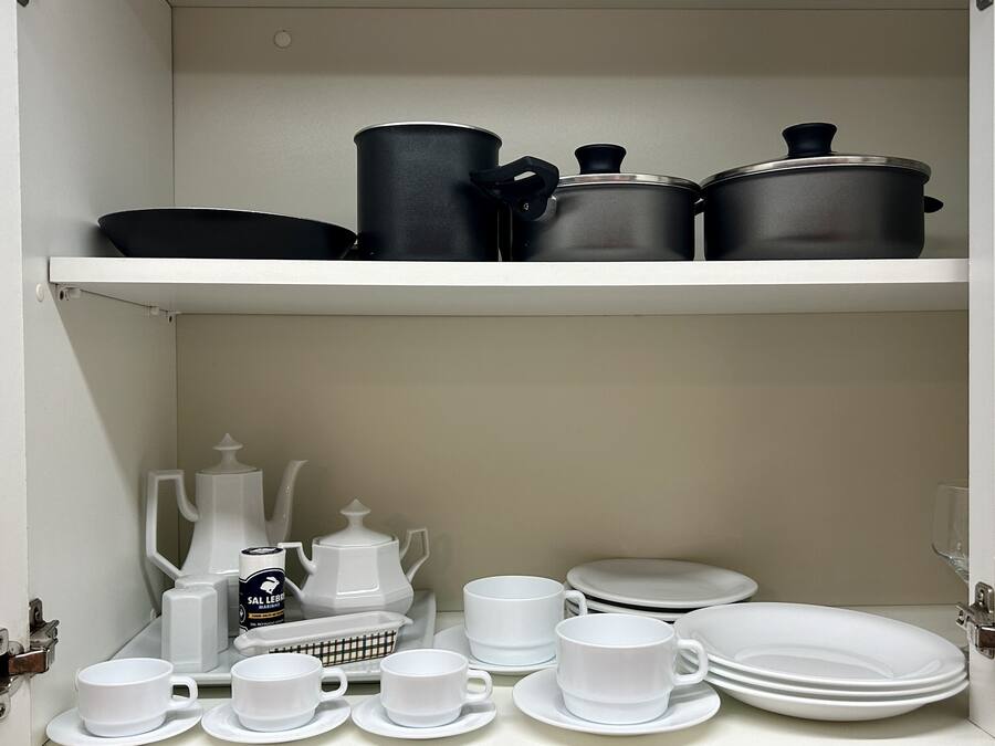 A kitchen cabinet with black and white cookware, a coffee maker, and white dishes.