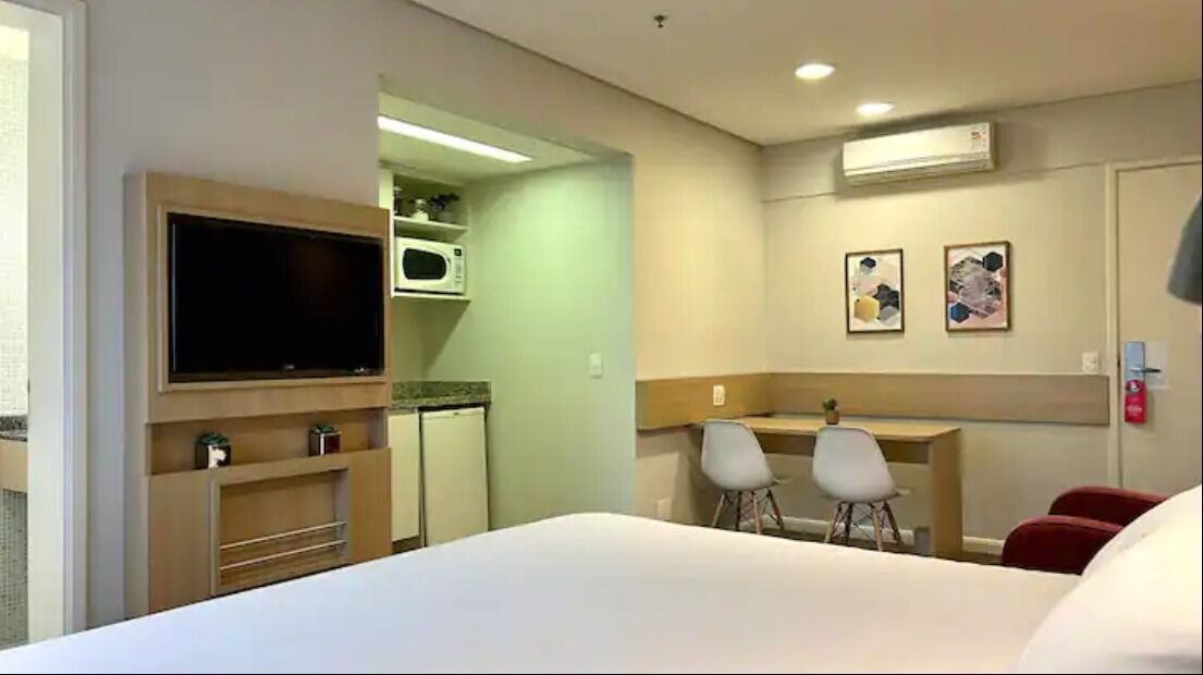A hotel room with a bed, a TV, a desk with two chairs, a microwave, and a small refrigerator.