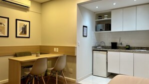 Cocina compacta con armarios blancos, encimera de granito y microondas integrado. Cuenta con un pequeño comedor con una mesa de madera y dos sillas.