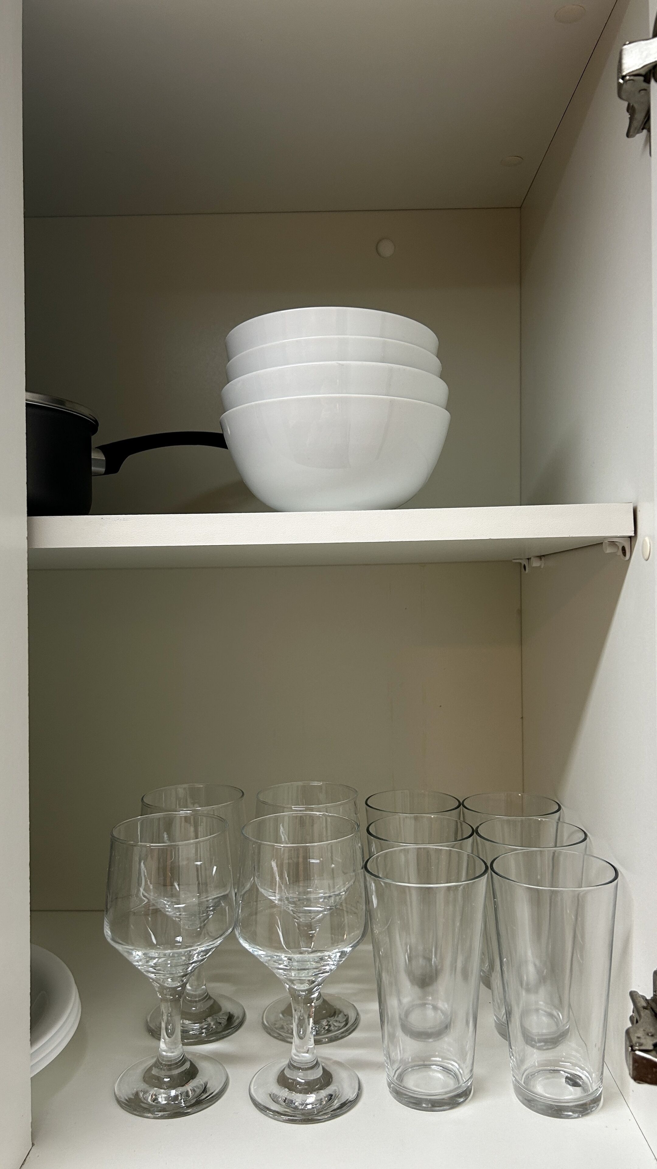 A white shelf with stacked white bowls and clear wine glasses.