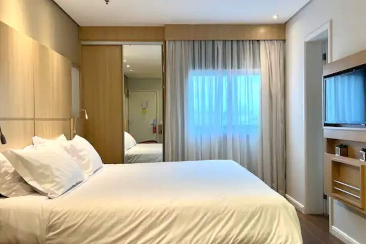 A modern hotel room with a large bed, a TV, and a wardrobe.
