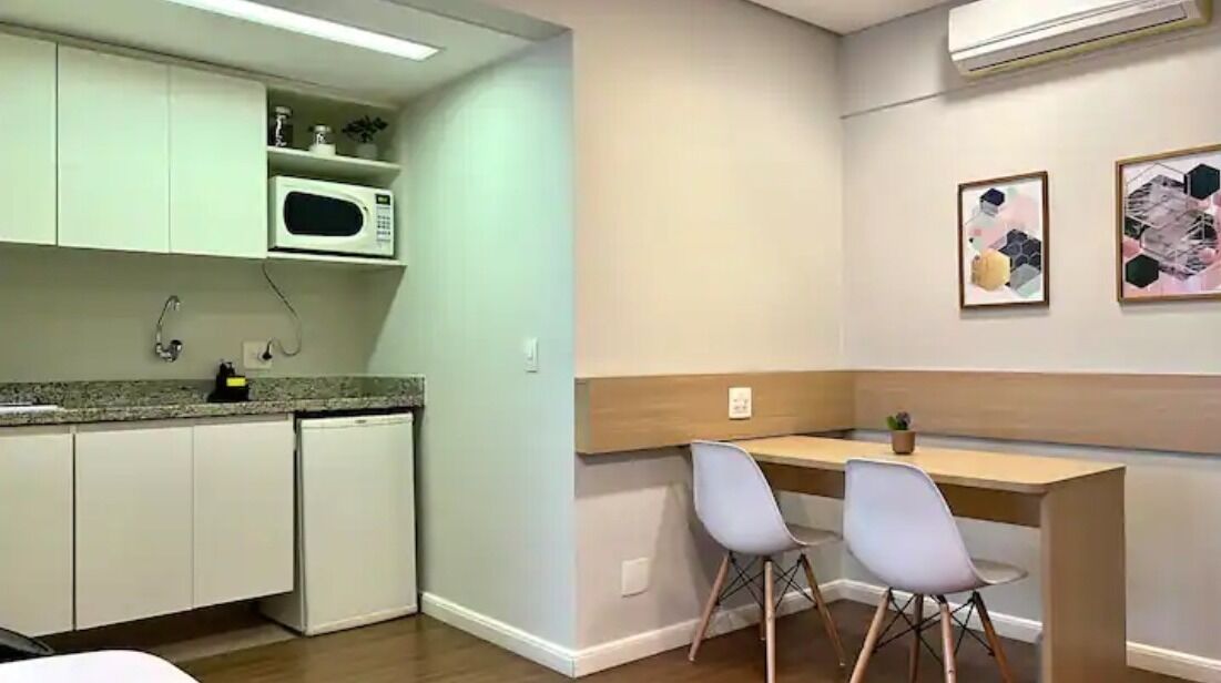 A compact kitchen with white cabinets, a microwave, and a small sink. There are two chairs at a wooden table, and the room has light-colored walls and a ceiling fan.