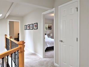 A hallway with a staircase, a bed, and a door.