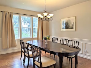 A dining room with a large round table, six chairs, a chandelier, and a framed picture on the wall.