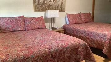 Quarto de hotel com duas camas, cada uma com colcha estampada, uma mesa de cabeceira com abajur e uma obra de arte pendurada na parede.