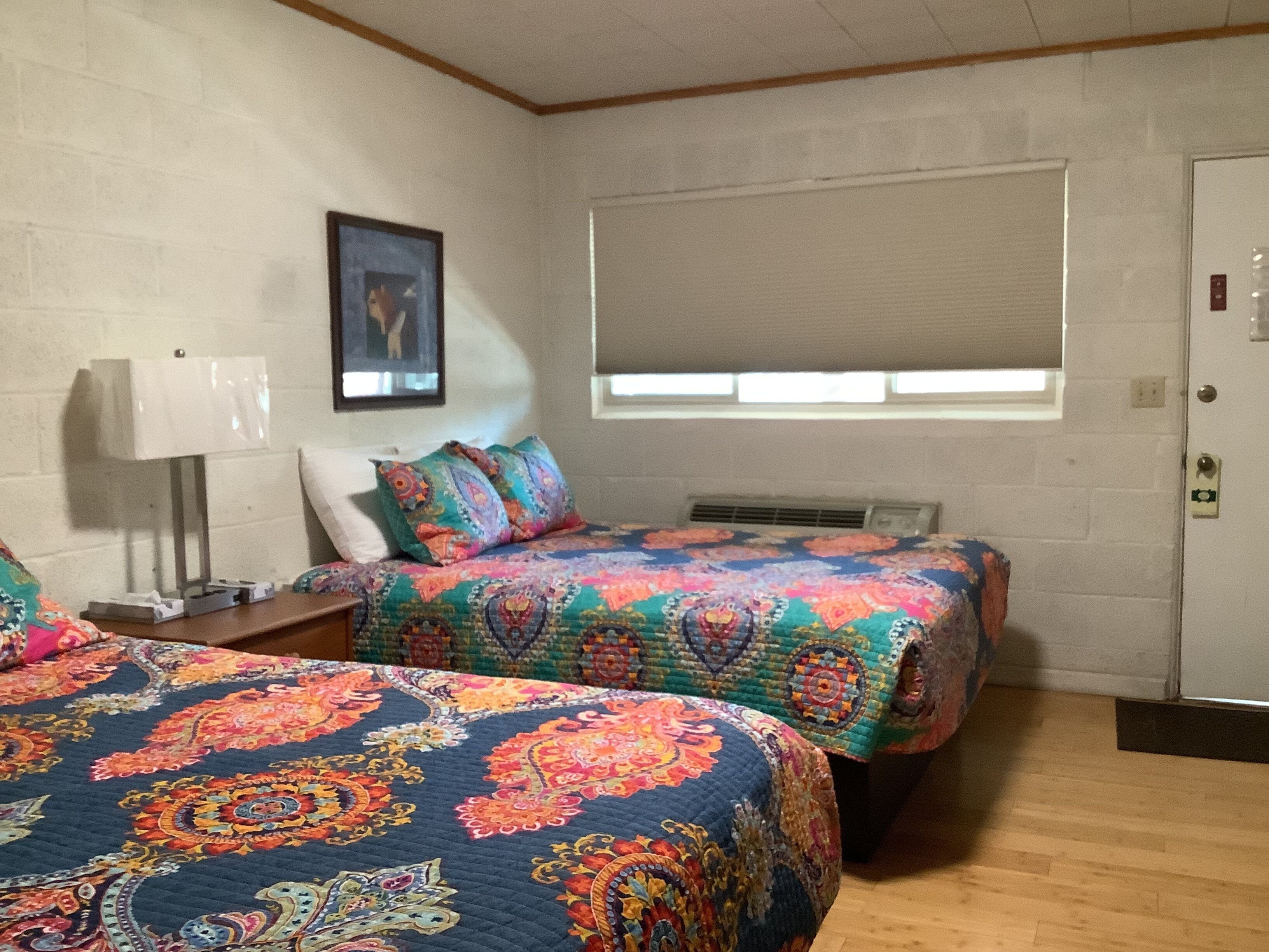 Ein Zimmer mit zwei Betten, einem Fenster mit Jalousien, einer Wandklimaanlage und einer Tür mit Schloss.