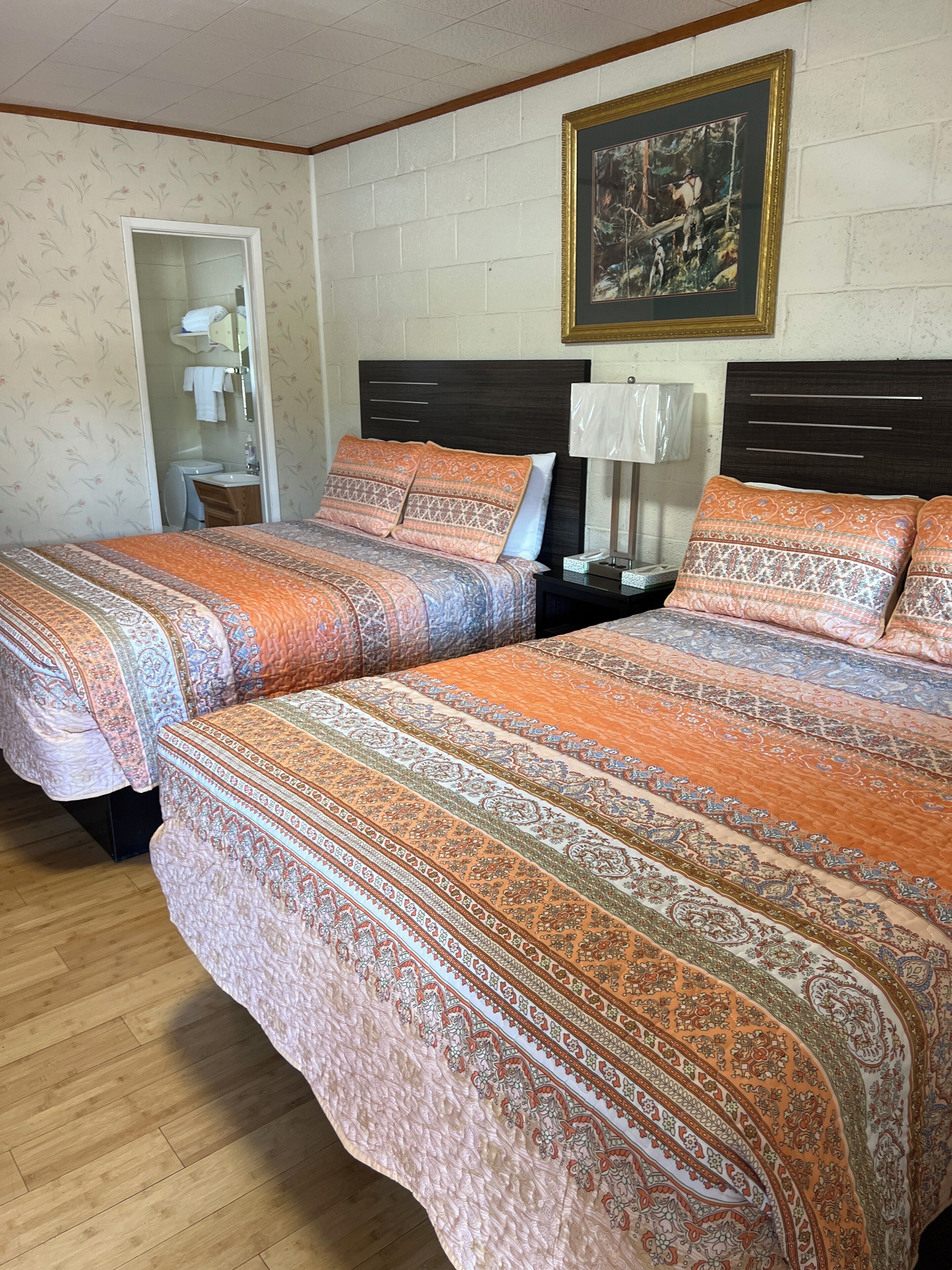 A double bed with patterned bedding, a nightstand with a lamp, and a framed picture on the wall.
