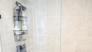 Una doccia con porta in vetro, un portascopevoli e un piccolo ripiano con articoli da bagno.