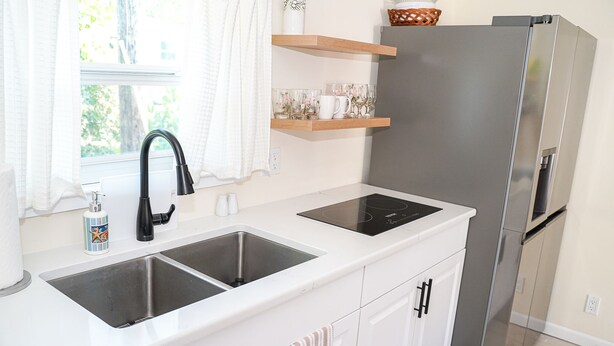 Una cucina moderna con frigorifero in acciaio inossidabile, lavello doppio e mensole in legno sopra il bancone.