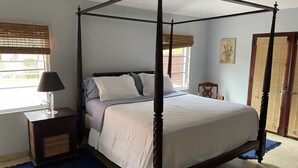 A four-poster bed with a white bedspread and pillows, a bedside table with a lamp, and a window with blinds. - Walk to the beach (Christiansted)