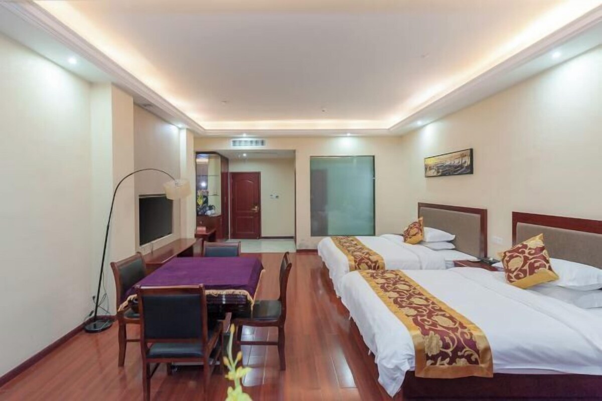 A hotel room with two beds, a desk, a chair, a television, and a door leading to another room.