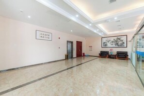 A hotel lobby with a marble floor, a reception desk, a framed artwork on the wall, and a door leading to another room. - Yin He Hotel (Zunyi)