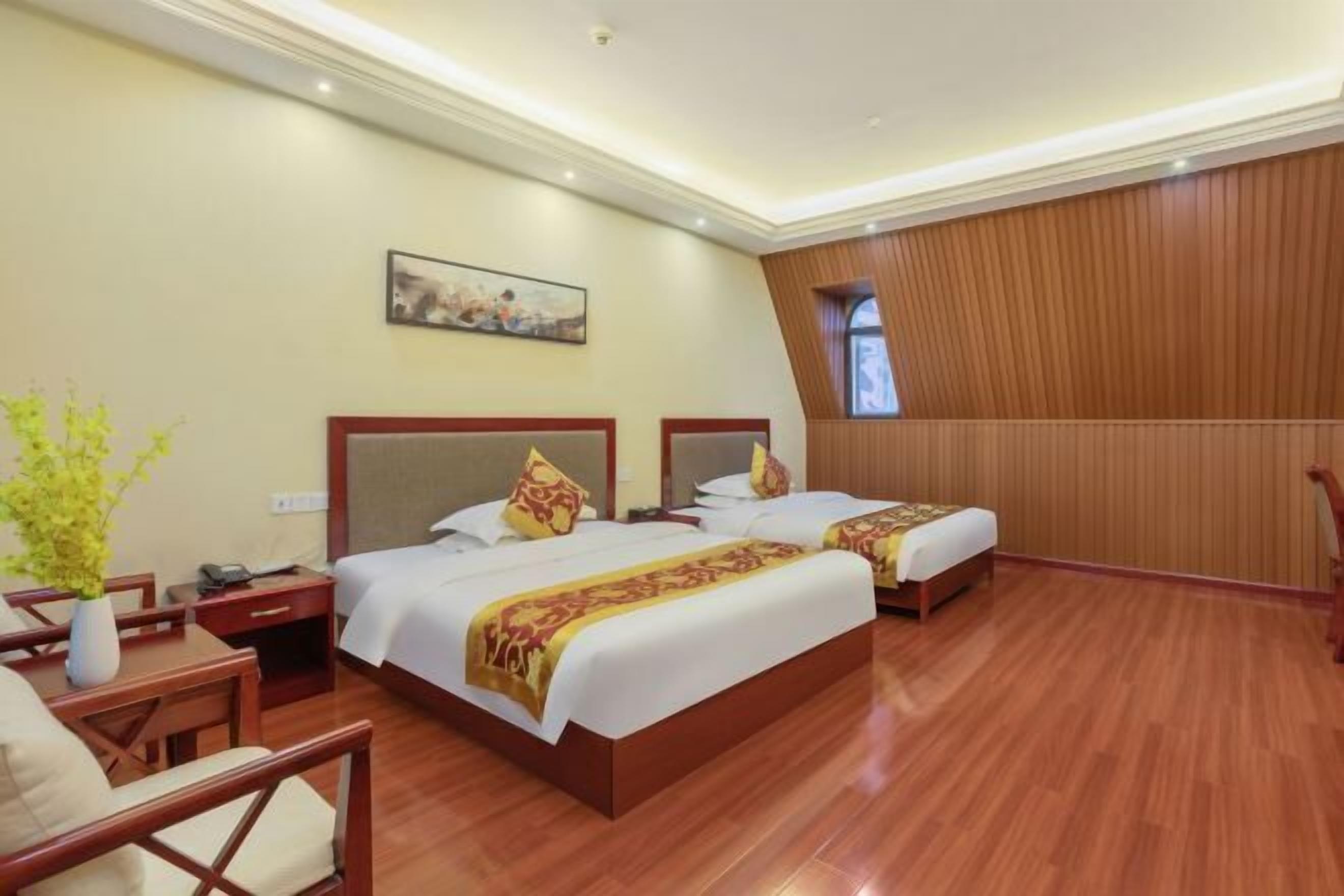 A hotel room with two beds, a desk, a chair, a small table, and a painting on the wall.