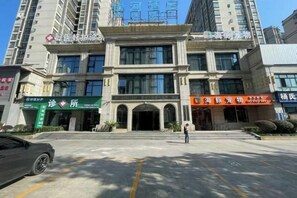 A multi-story building with a central entrance, several storefronts on the ground floor, and a parking lot in the foreground. - Yin He Hotel (Zunyi)