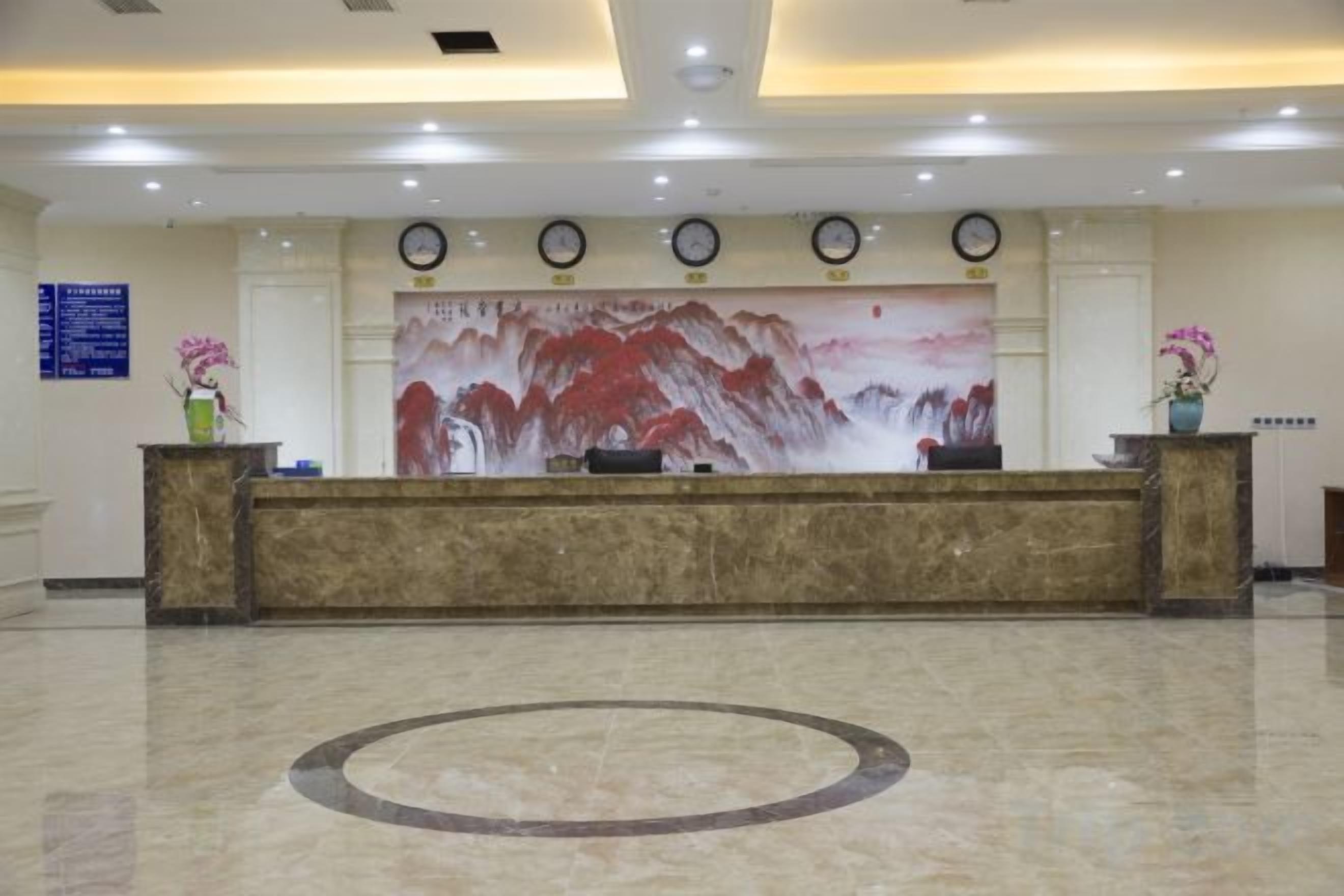 A hotel reception area with a marble reception desk, a large wall painting, and a clock on the wall.