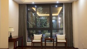 A room with a large window, two chairs, a small table, and a lamp. - Yin He Hotel (Zunyi)