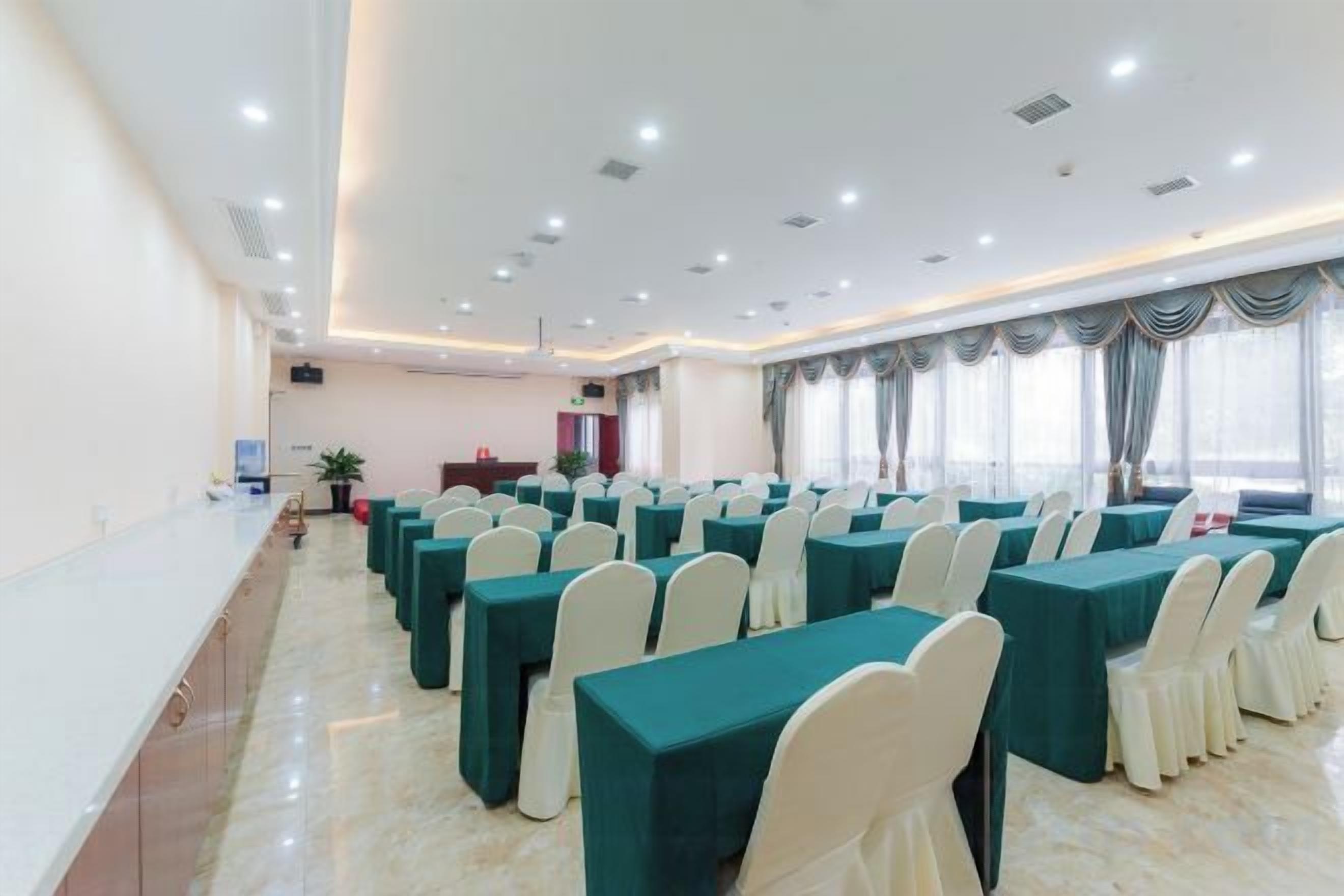 Une salle de conférence avec des rangées de tables et de chaises, un pupitre et une grande fenêtre avec des rideaux.