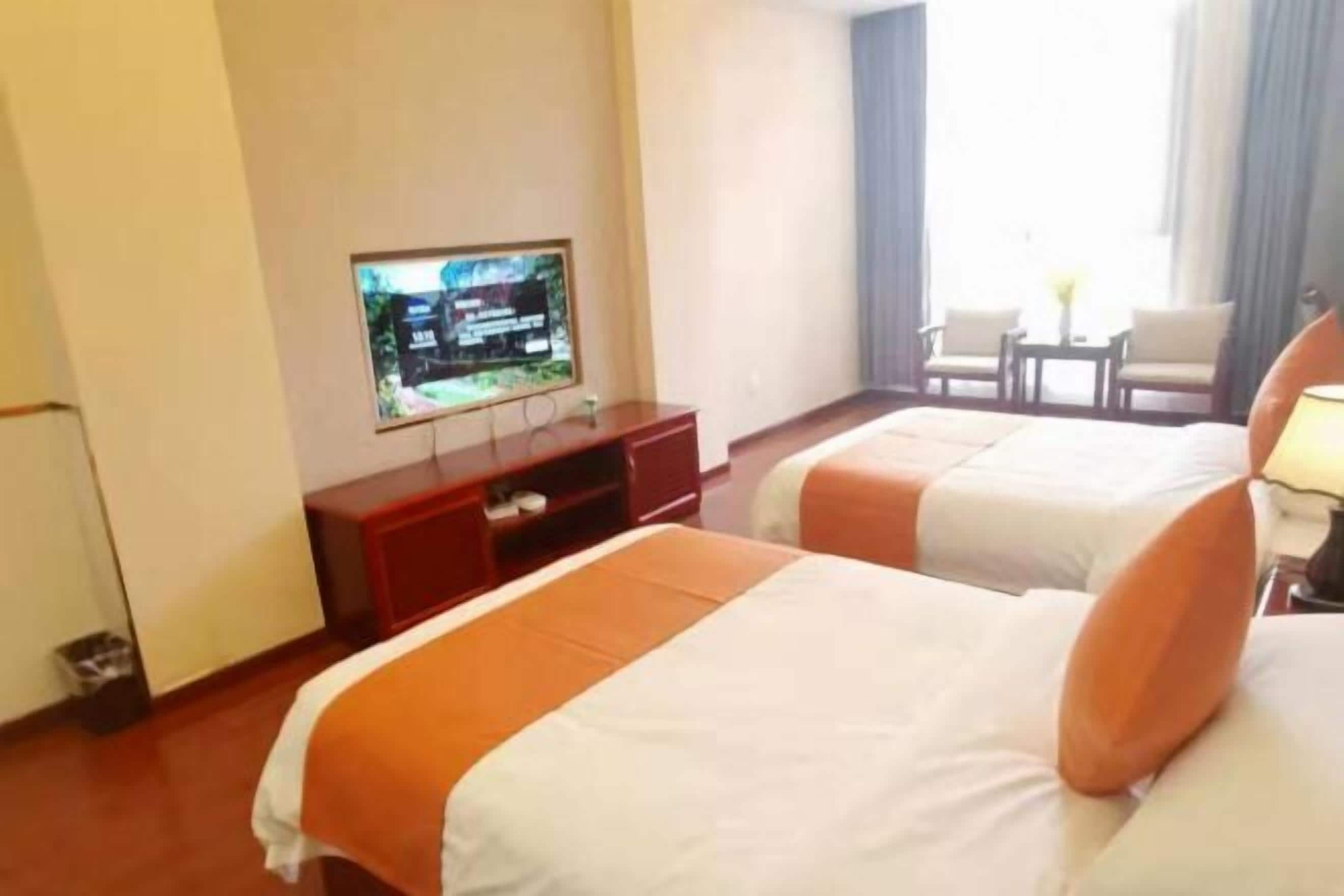 A hotel room with two beds, a TV on a stand, a small table, and a window with curtains.