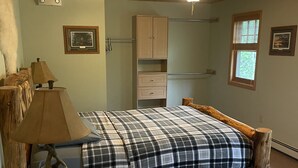 A wooden bed with a plaid blanket, a wooden nightstand with a lamp, a wooden chair, a wooden desk, a window with blinds, and a ceiling fan. - Beautiful 2 bedroom house  with a boat dock on the Chippewa Flowage  (Hayward)
