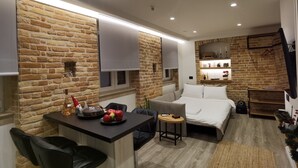 Une chambre d’hôtel moderne avec un mur en briques, un lit, un bureau avec une chaise, une petite table et un luminaire suspendu.
