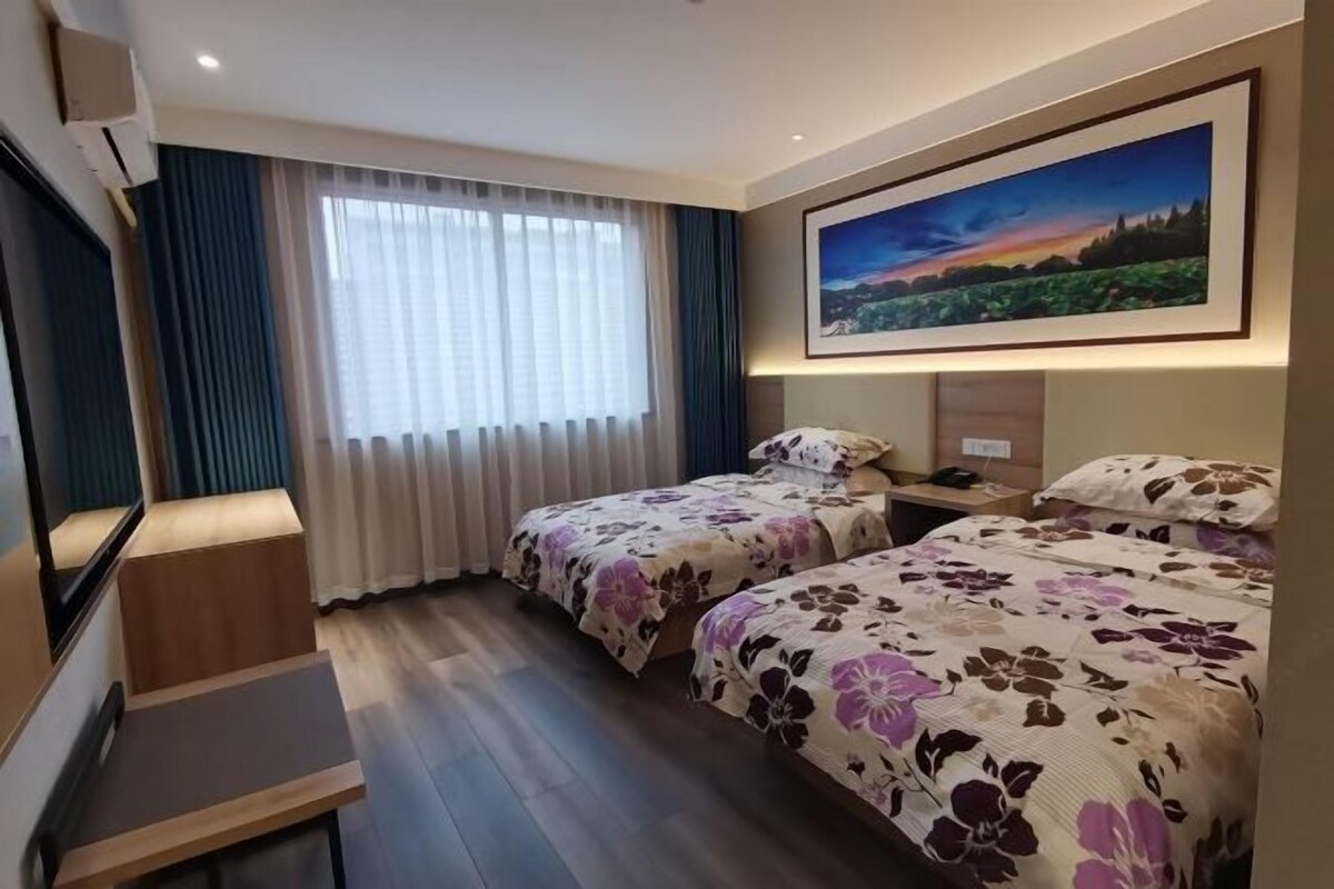 A hotel room with two beds, a desk, a TV, and a painting on the wall.