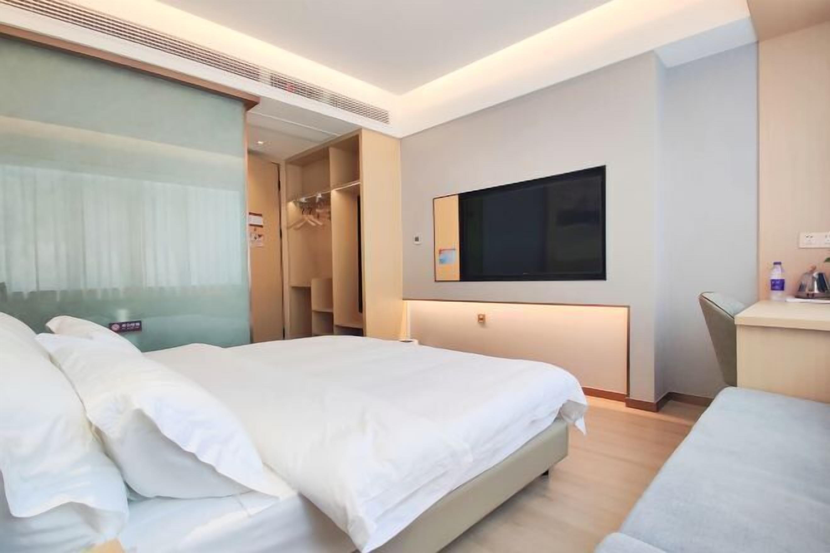 Quarto de hotel com cama, televisão na parede, escrivaninha e guarda-roupa.