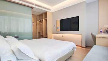 Quarto de hotel com cama, televisão na parede, escrivaninha e guarda-roupa.