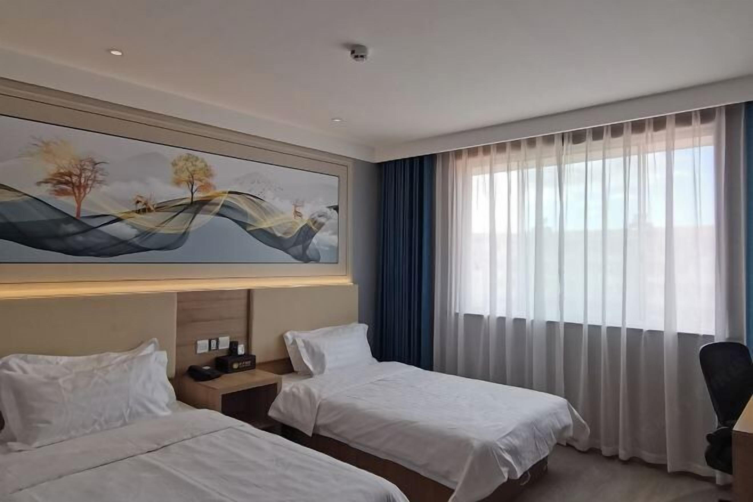 Habitación de hotel con dos camas, un cuadro en la pared, una mesita de noche, un escritorio y una ventana con cortinas.