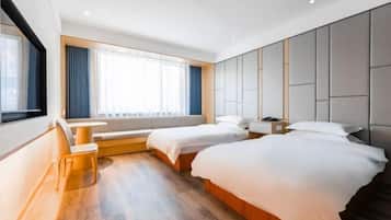 Quarto de hotel moderno com duas camas, área de estar e uma janela grande com cortinas.
