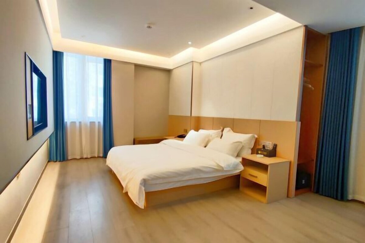 A modern hotel room with a large bed, bedside tables, a wardrobe, and a window with curtains.
