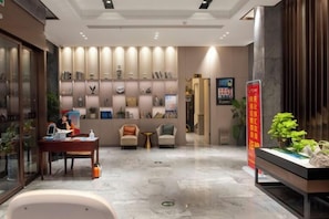 A hotel lobby with a reception desk, seating area, and decorative wall shelves. - Guyue Hotel (Shengzhou Wuyue Plaza Branch) (Shengzhou)