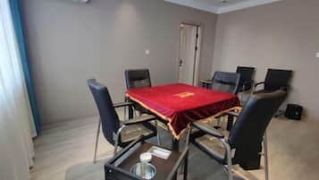 Un salón de conferencias con una mesa roja, seis sillas, una mesa pequeña con un bol y una servilleta, y una puerta al fondo.