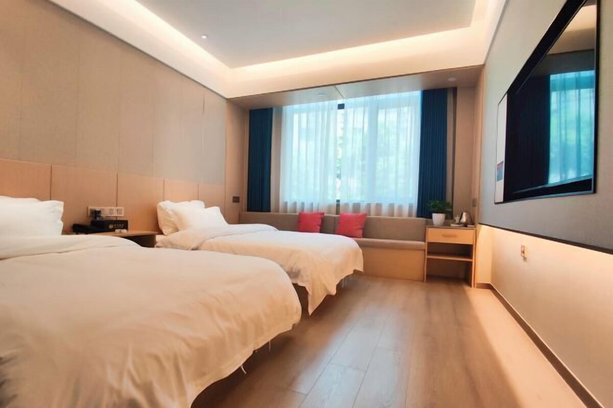 A hotel room with two beds, a desk, a window with curtains, and a large mirror.