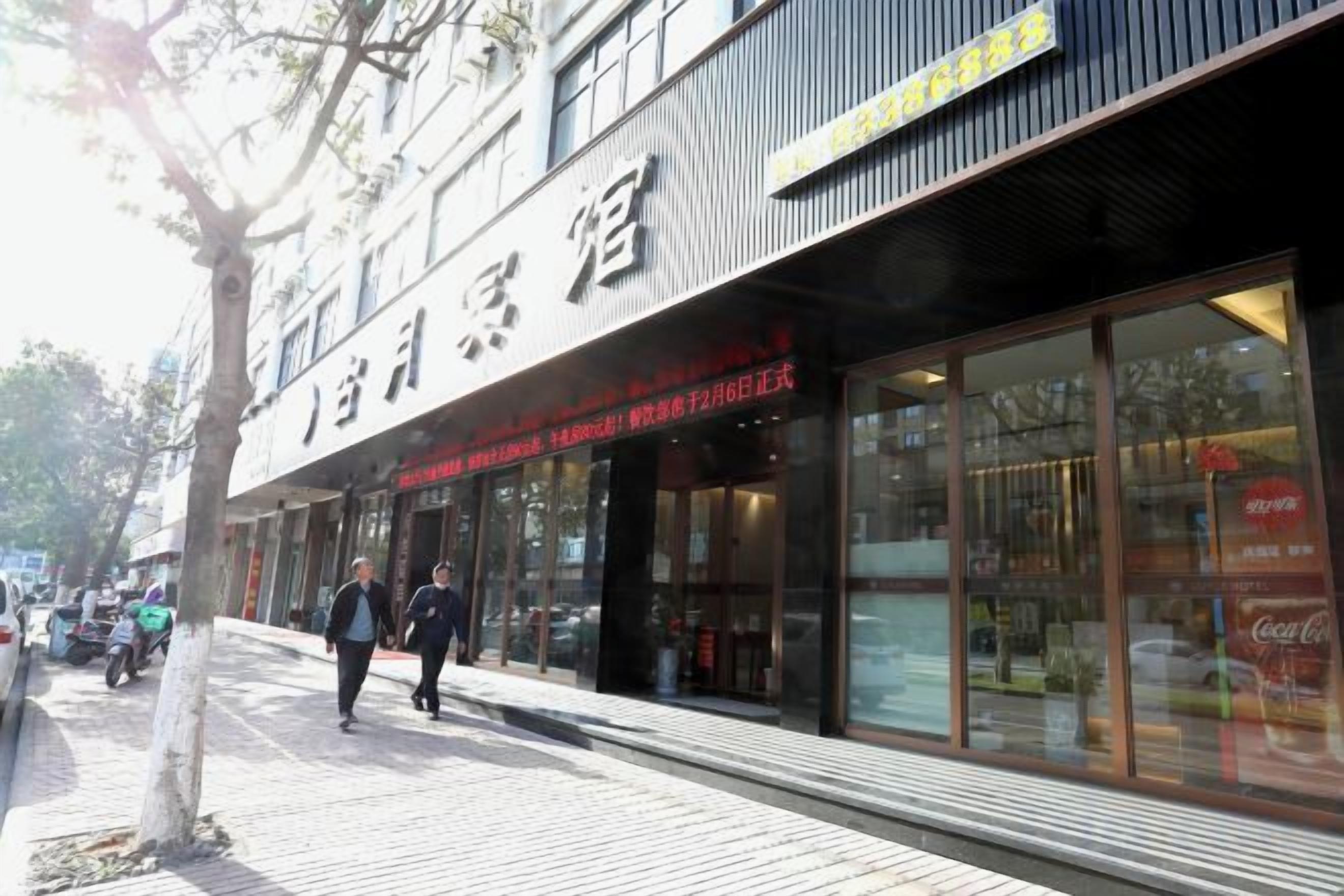 A hotel facade with large glass windows, a visible entrance, and a signboard.