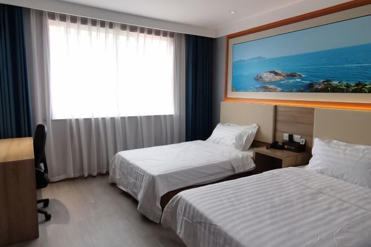 A hotel room with two beds, a desk, and a large window with curtains.