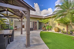 Un patio cubierto con mobiliario exterior, un césped bien cuidado y una maceta decorativa grande.