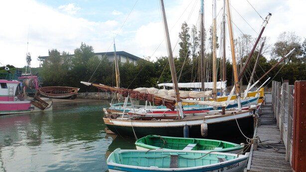A marina with several boats docked, a wooden pier, and a building in the background. - House 5 minutes from the beach and shops (La Brée-les-Bains)