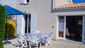 A two-story house with a patio area featuring a table and chairs, a satellite dish, and a blue umbrella. - House 5 minutes from the beach and shops (La Brée-les-Bains)