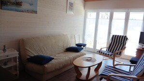 A living room with a beige sofa, a striped armchair, a small round table, and a television on a wooden stand. - House 5 minutes from the beach and shops (La Brée-les-Bains)