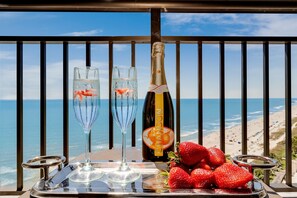 Un balcón con vista a la playa, dos copas de champán, una botella de champán Chandon y fresas frescas en una bandeja.