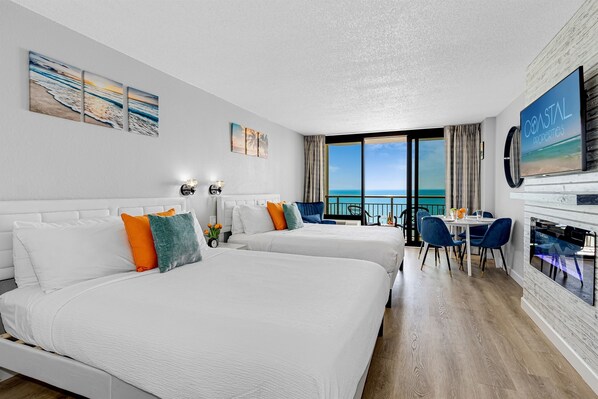 Habitación de hotel con dos camas, un área de comedor y un ventanal con vista al océano.