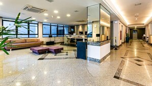 A modern hotel lobby with a reception desk, seating area, and large windows. - Rooftop Pool with Sea and Bridge Views #CA22 (Florianópolis)