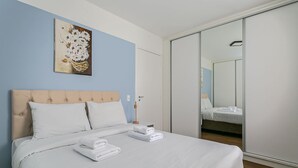 Een keurig opgemaakt bed met witte lakens en handdoeken, een hoofdbord en een bloemen schilderij aan de muur.