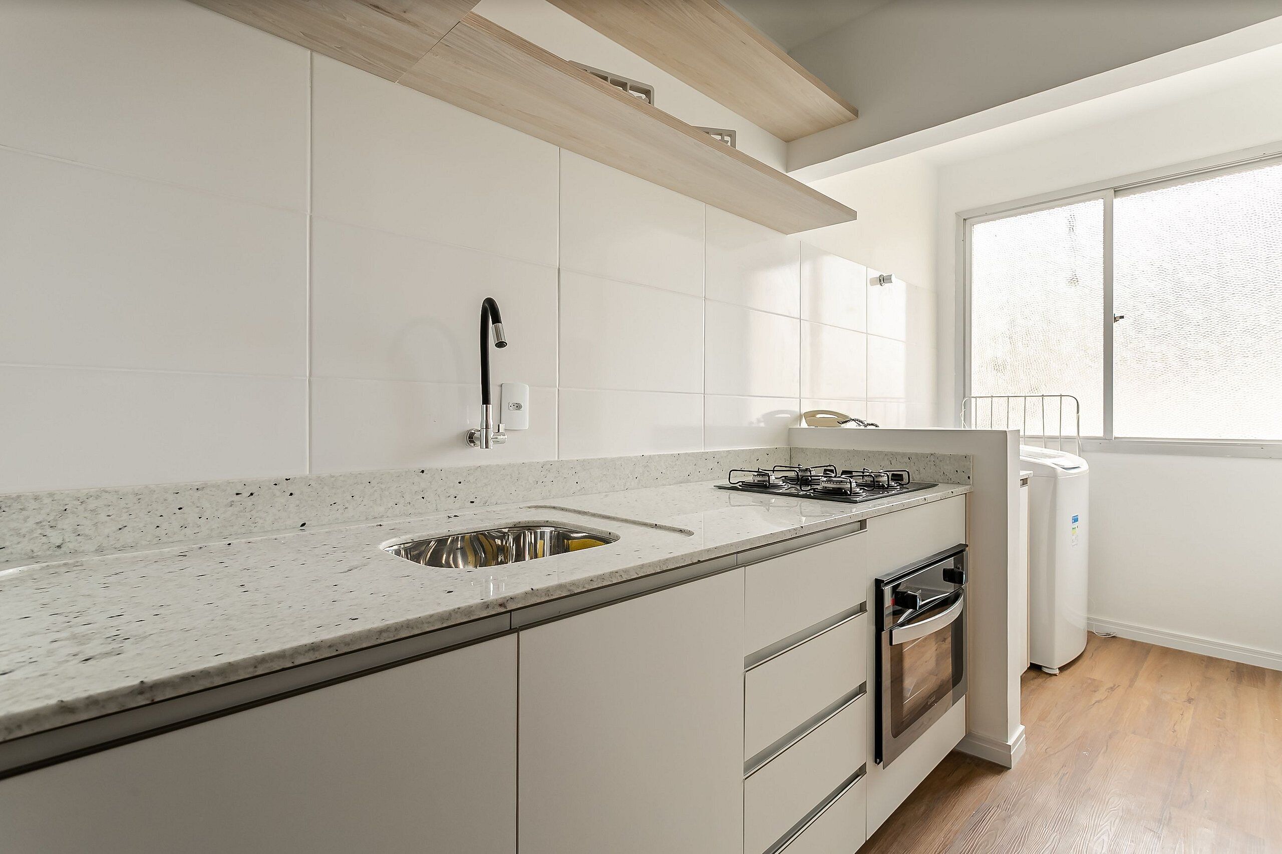 Una cocina moderna con armarios blancos, encimera de granito, horno empotrado y ventana que proporciona luz natural.